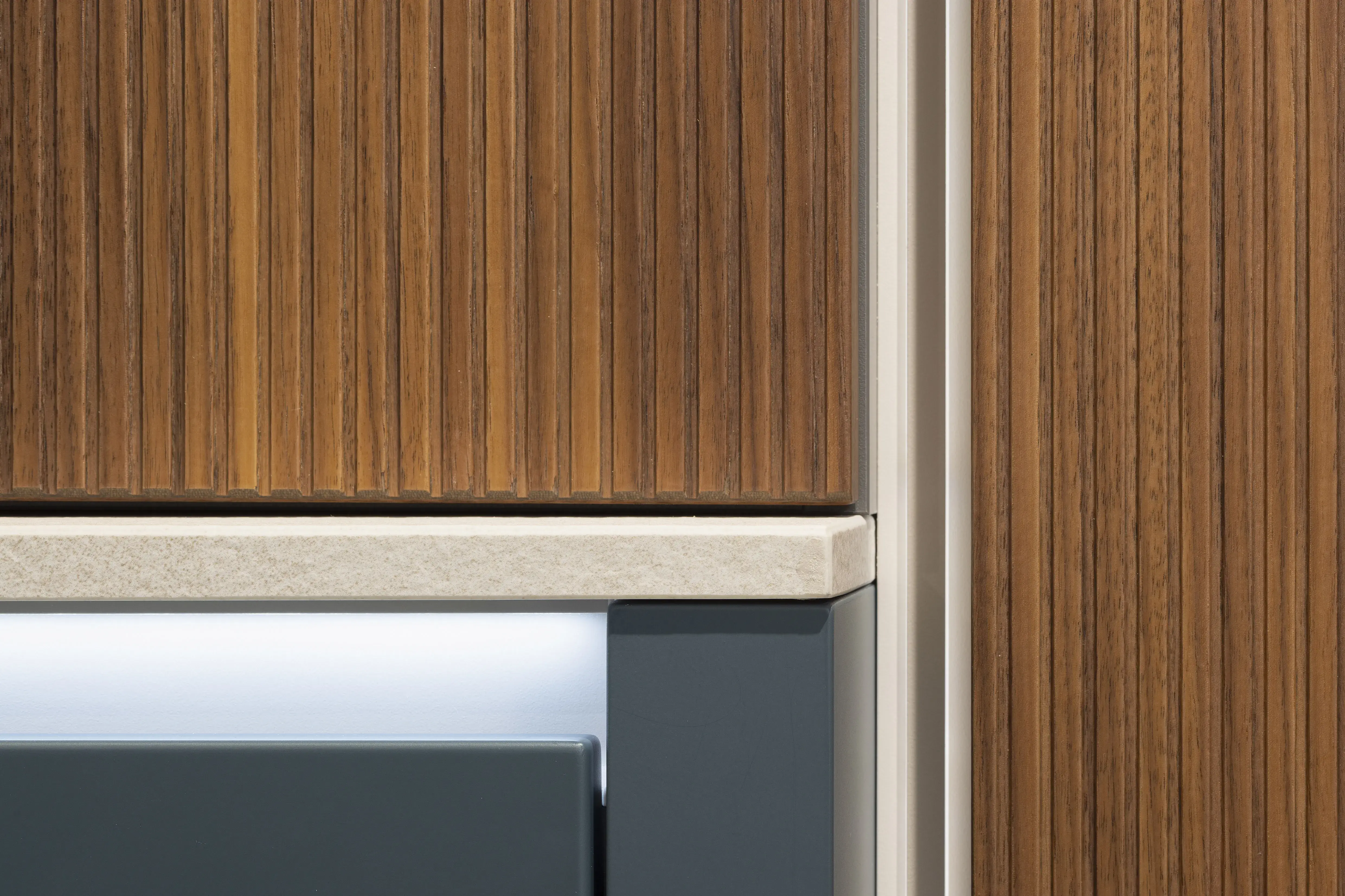 Moderne Küchenfront aus Holz mit heller Arbeitsplatte und LED-Lichtleiste